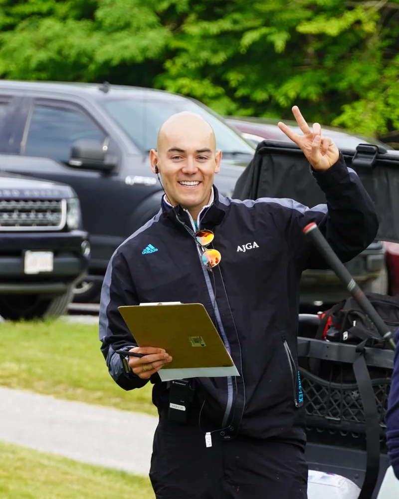 Clay on the course at an American Junior Golf Association event, holding a clipboard and flashing a peace sign.
